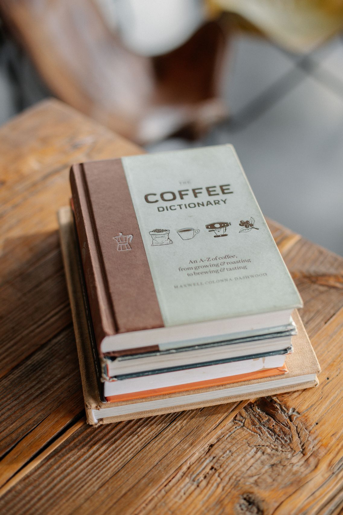 Stack of hardcover books next to a coffee mug and a small vase of flowers
